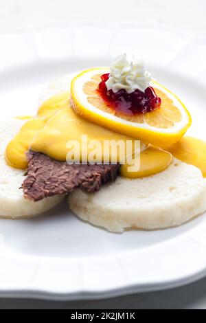 Sirloin-Sahnesauce mit Knödeln, serviert mit Zitrone, Preiselbeeren und Schlagsahne Stockfoto