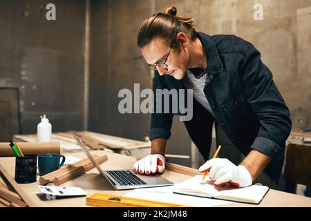 Ich denke, meine Berechnungen sind richtig. Ausgeschnittene Aufnahme eines fokussierten jungen Zimmermanns, der nachts in einer Werkstatt an einem Projekt arbeitet. Stockfoto