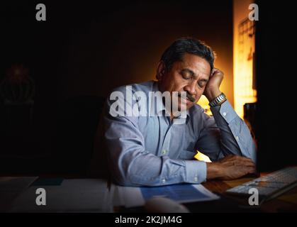 Die langen Stunden haben ihn erschöpft. Aufnahme eines reifen Geschäftsmannes, der an seinem Schreibtisch schläft, während er spät in einem Büro arbeitet. Stockfoto