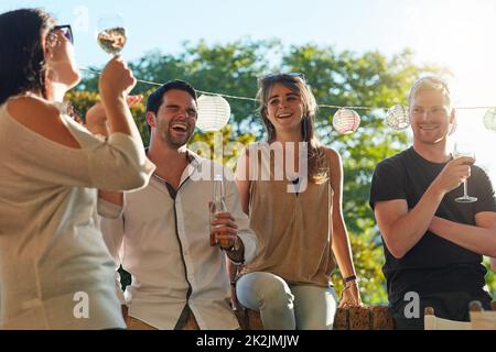 Genießen Sie Wein in der Sonne. Aufnahme einer Gruppe glücklicher junger Freunde, die auf einer Hinterhof-Dinner-Party rumhängen. Stockfoto