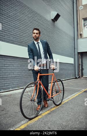 Hes war sich immer bewusst, wie er pendelt. Aufnahme eines hübschen jungen Geschäftsmannes, der neben seinem Fahrrad im Freien steht. Stockfoto