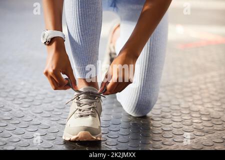 Treten Sie in den Kreis der Gewinner ein. Aufnahme einer unkenntlichen Frau, die ihre Schnürsenkel vor einem Training im Fitnessstudio bindet. Stockfoto