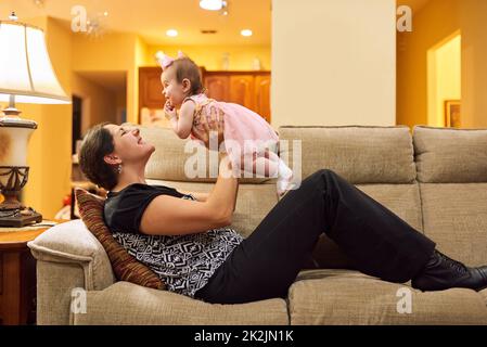 Bindung mit meinem Baby. Eine kleine Aufnahme einer Mutter, die ihre entzückende kleine Tochter auf der Couch im Wohnzimmer zu Hause abholt. Stockfoto