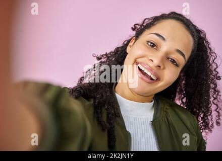 Verspielt wird nie aus der Mode kommen. Aufnahme einer attraktiven jungen Frau, die allein vor einem rosa Hintergrund im Studio steht und ein Selfie macht. Stockfoto