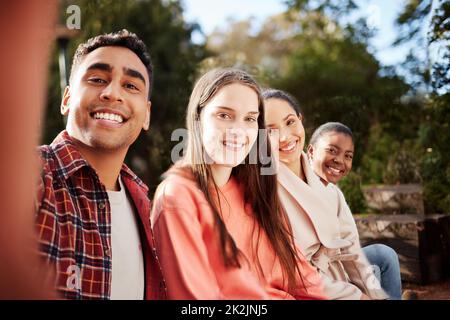 Freunde auf dem Campus. Porträt von vier jungen Universitätsstudenten, die während ihrer Pause Selfies machen, während sie draußen auf dem Campus sitzen. Stockfoto