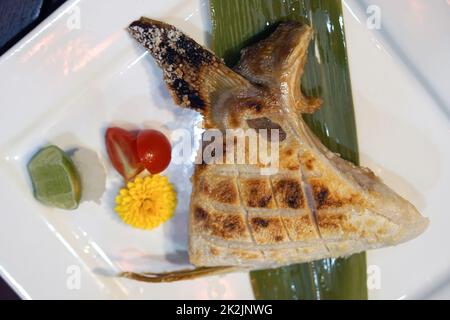 Hamachi Kama Shio serviert auf weißem Teller mit Zitrone und Tomaten. Holzkohle gegrillte Hamachi Fischbäche mit Salz. Japanische Kochtechnik: Shioyaki Stockfoto