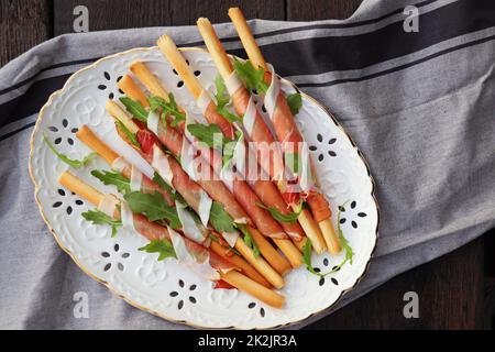 Antipasto-Platte kalte Fleischplatte mit Grissini-Brotscheiben, Prosciutto, Schinkenscheiben und Rucola auf Holzboden. Vorspeise mit Fleisch. Draufsicht Stockfoto