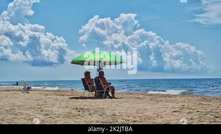 Ein älteres Paar unter einem Sonnenschirm am Strand Stockfoto