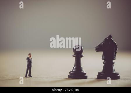 Miniaturgeschäftsmann vor Schachfiguren. Geschäftskonzept Stockfoto