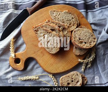 Frisch gebackenes, geschnittenes Roggenbrot auf Holzschneidebrett mit Körnern, flach liegend Stockfoto