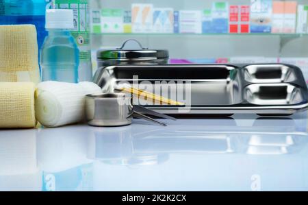 Wundpflegeset und Edelstahlplatte, Pinzette, Jodbecher, passender Verband, elastischer bindender Verband, antiseptische und normale Kochsalzflasche auf verschwommenen Medikamentenregalen in Apotheken. Stockfoto