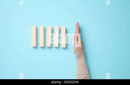 Hand stoppt den Fall von Holzblöcken auf einem blauen Hintergrund. Konzept einer starken und mutigen Persönlichkeit, die ungleichen Schwierigkeiten standhalten kann Stockfoto