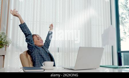 Glückliche Geschäftsfrau war begeistert und überraschte die Arbeit an einem weißen Büroschreibtisch mit pc-Laptop, der Papierdokumente auswarf Stockfoto