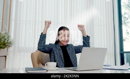 Glückliche Geschäftsfrau war begeistert und überraschte die Arbeit an einem weißen Büroschreibtisch mit pc-Laptop, der Papierdokumente auswarf Stockfoto