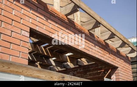 Ein im Bau befindliches privates Wohngebäude mit einer Dachkonstruktion mit Holzrahmen. Unbearbeitetes Ziegelgebäude im Bau, Nahaufnahme Stockfoto
