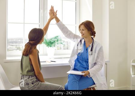 Fröhliche junge Ärztin gibt hohe fünf Teenager-Mädchen nach der medizinischen Untersuchung. Stockfoto