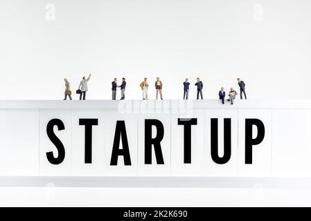 Startup-Konzept. Miniaturmenschen auf dem Leuchtkasten mit einem Wort Startup Stockfoto