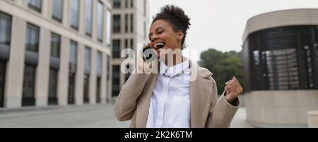 afroamerikanische Unternehmerin mit einem zufriedenen Gesicht und einem Lächeln spricht auf einem Handy nach einer erfolgreichen Transaktion auf dem Hintergrund eines Stockfoto