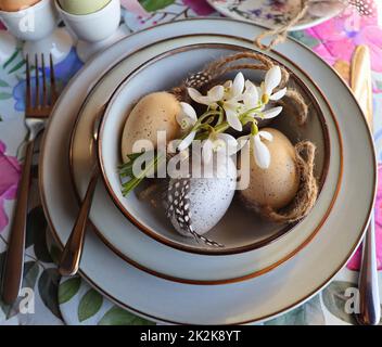 Stilvolles Ostertisch mit Ei in Schale auf Tisch. Modernes, natürlich gefärbtes osterei, Blumen auf Teller und Besteck. Ostern festliche Tischdekorationen Stockfoto