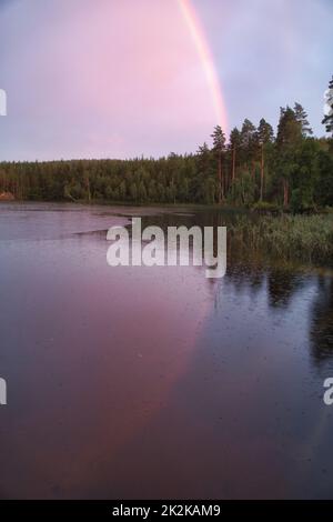 Regenbogen spiegelte sich im See, wenn es regnet. Im Hintergrund Wald, auf dem See Schilf und Seerosen. Naturfotos aus Schweden Stockfoto