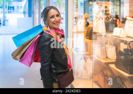 Attraktive Dame mit Einkaufstaschen glücklich lächelnd Blick zur Kamera vor einem Geschäft. Weihnachtseinkäufe. Stockfoto