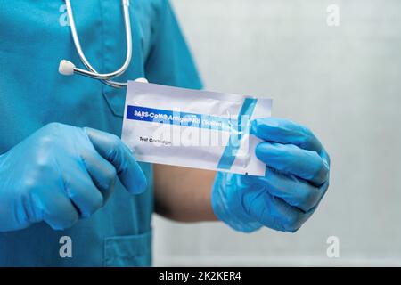 Ein asiatischer Arzt im PSA-Anzug zeigt ein positives Testergebnis mit dem Speichelantigen-Testkit zur Kontrolle des Covid-19-Coronavirus im Krankenhaus. Stockfoto