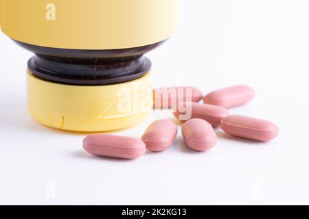 Rosa Pillen aus einem Plastikglas auf weißem Hintergrund verstreut Stockfoto