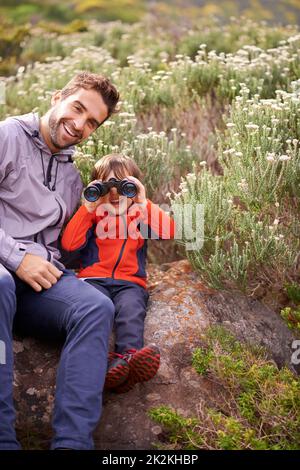 Es wartet eine ganze Welt darauf entdeckt zu werden. Ein kleiner Junge schaut durch ein Fernglas, während er mit seinem Vater unterwegs ist. Stockfoto