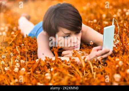 Junge Frau, die auf einer Wiese liegt und auf ihrem Handy eine Melodie auswählt Stockfoto