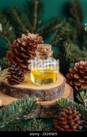 Glasflasche mit ätherischem Koniferöl in der Nähe von Tannenzweigen und Kiefernzapfen auf grünem Nahbild Stockfoto