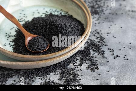 Teller mit indischem Gewürz Schwarzer Kreuzkümmel (Nigella sativa oder Kalonji), Nahaufnahme mit einem Holzlöffel Stockfoto