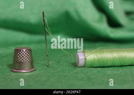 Spule aus grünem Faden, Nimble und Nadel auf grünem Stoff Stockfoto