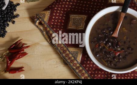 Black Bean Chili auf Holztisch mit Gewürzen und getrockneten schwarzen Bohnen Stockfoto