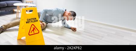 Mann, Der Auf Nassen Boden Fällt, Vor Dem Warnschild Stockfoto