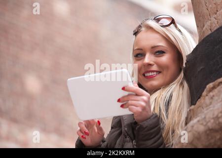 Blondes lächelndes Mädchen mit einem Tablet im Freien Stockfoto