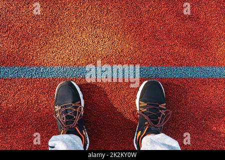 Füße in Sneakers stehen auf der Laufstrecke mit blauer Linie Stockfoto