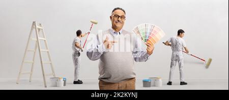 Reifer Mann mit einer Farbpalette und Maler malen eine Wand im Hintergrund Stockfoto