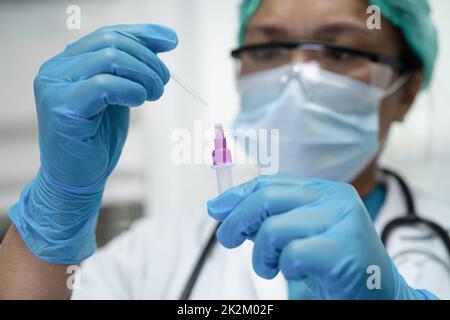 Ein asiatischer Arzt im PSA-Anzug zeigt ein positives Testergebnis mit dem Speichelantigen-Testkit zur Kontrolle des Covid-19-Coronavirus im Krankenhaus. Stockfoto