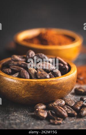Kakaobohnen und Kakaopulver in Holzschüsseln auf schwarzem Tisch. Stockfoto