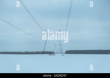 Hochspannungsmasten Winter. Strom für Städte. In der Mitte eines schneebedeckten Feldes stehen elektrische Pylons. Das Konzept der Heizung, Heizung und al Stockfoto