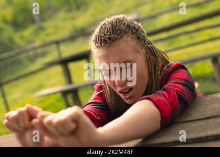 Eine Frau, die Arme über einen Tisch streckt und im Park gähnt Stockfoto