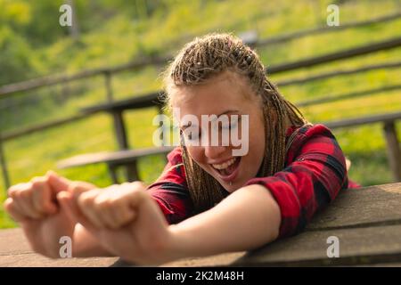 Eine Frau, die Arme über einen Tisch streckt und im Park gähnt Stockfoto