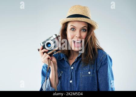 Ich kann mir keinen aufregenderen Moment vorstellen. Studioportrait einer jungen Frau mit einer Vintage-Kamera vor grauem Hintergrund. Stockfoto