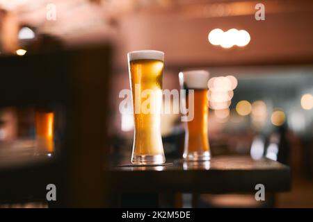 Nehmen Sie die Ladung mit einem Glas Bier. Aufnahme von zwei Gläsern Bier, die tagsüber an einem Tisch in einer Bierbrauerei stehen. Stockfoto