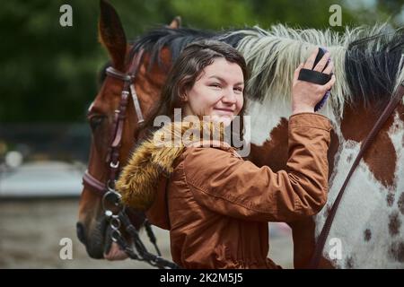 Wer auch immer sagte, dass man Glück nicht kaufen kann, hatte nie ein Pony. Aufnahme eines Teenagers, das sich auf einer Farm die Ponys putzt. Stockfoto