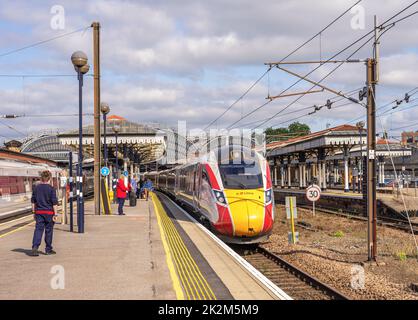 Ein Zug ruht auf einer Plattform mit einem historischen Vordach. Crew-Mitglieder und Passagiere stehen auf dem Bahnsteig. Ein Himmel mit Wolken ist oben. Stockfoto