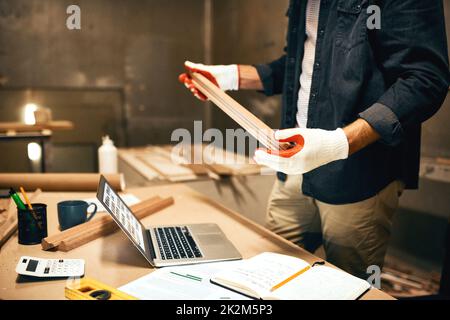 Dies ist definitiv die richtige Holzart. Gekürzte Aufnahme eines unbekannten Zimmermanns, der ein Stück Holz hält und untersucht, während er nachts in einer Werkstatt arbeitet. Stockfoto