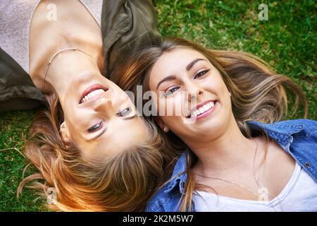 Freunde sind das, was den Sommer wirklich macht. Hochwinkelporträt von zwei attraktiven jungen Frauen, die draußen auf dem Gras liegen. Stockfoto