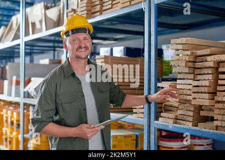 Alles, was ich brauche, ist hier genau richtig. Ein beschnittenes Porträt eines hübschen, reifen Bauarbeiters, der sein Tablet benutzte, während er in einem Industrielager stand. Stockfoto