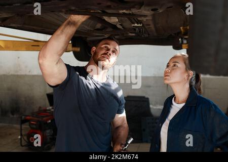 Erstklassiger Service ist unser wichtigstes Fahrzeug. Aufnahme von zwei Mechanikern, die unter einem angehobenen Auto zusammenarbeiten. Stockfoto